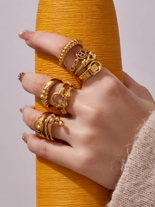 Close-up of golden geometric rings with buckle and chain details on a yellow prop