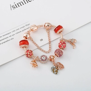 Bracelet maille serpent or rose avec perles rouges et breloques feuilles sur magazine