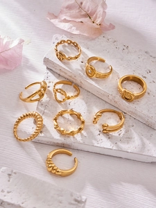 Macro shot of gold geometric open rings featuring a letter B and knot motifs on stone