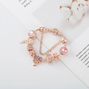 Détail du bracelet à breloques en or rose avec cristaux roses, cœur et chaîne serpent