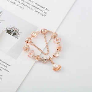 Détail d'un bracelet à breloques or rose avec perles en verre rose et pendentifs cœur