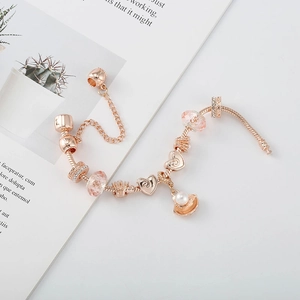 Détail du bracelet charms or rose avec perles en verre rose et coquillage sur maille serpent
