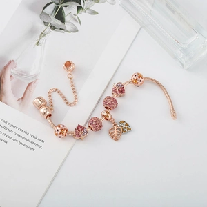 Gros plan d'un bracelet maille serpent or rose avec charms en cristal rose et motifs fleurs