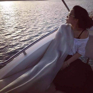 Close-up of a soft light grey ribbed knit shawl wrap against a scenic ocean backdrop