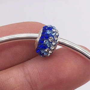 Macro detail of a cylinder charm bead featuring gradient blue and clear pavé crystals