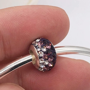 Detailed macro view of purple and pink pavé crystal charms on a silver bracelet band
