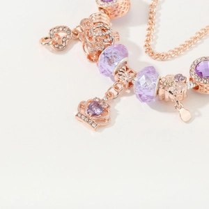 Rose gold charm bracelet featuring purple crystals, crown pendant, and heart charms
