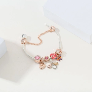 Detail of rose gold snake chain bracelet with pink faceted stones and lucky charms