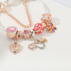 Close-up of rose gold charms with pink enamel butterfly and ladybug on silver snake chain