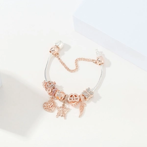 Rose gold snake chain bracelet with heart, feather, and butterfly charms on white props