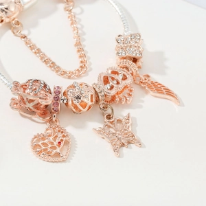 Detail of rose gold charm bracelet with butterfly, tree of life, and crown beads