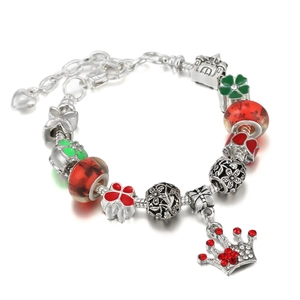 Close-up of silver snake chain bracelet with red glass beads and green enamel charms