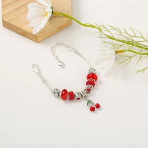 Macro detail of silver-plated snake chain bracelet with red beads and cherry charm pendant