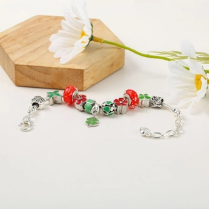 Detailed macro view of a silver snake chain bracelet with red and green floral charms