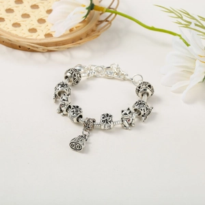 Silver snake chain bracelet with Lucky Cat and fortune bag charms on a textured mat