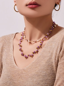 Close-up of layered necklace set featuring purple crystal stones and white pearls on a model