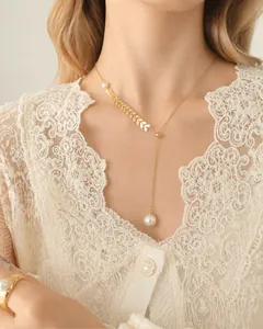 Detail of a 18k gold Y-shaped necklace with elegant gold leaves and a white pearl pendant