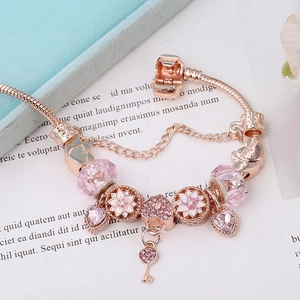 Pulsera de oro rosa con cuentas de vidrio rosa y dijes de flores sobre fondo blanco