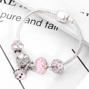 Silver charm bracelet with pink ladybug pendant and floral glass beads on white paper