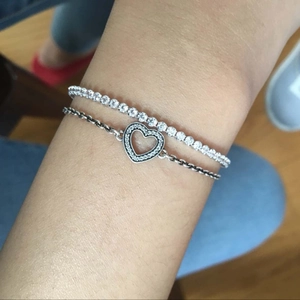 Primer plano de una pulsera tenis plateada y una pulsera de corazón en la muñeca mujer