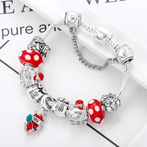 Macro detail of red glass beads and lucky charms on silver snake chain bracelet