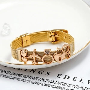 Detail of a 10mm gold mesh charm bracelet featuring heart, airplane, and ring pendants