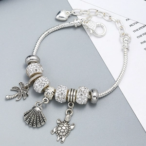 Macro detail of silver ocean-themed charm bracelet with palm tree and turtle pendants