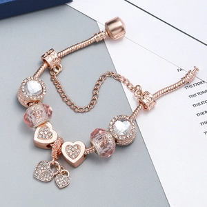 Rose gold snake chain bracelet with pink glass beads and heart charms on a box