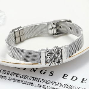 Detail of silver mesh bracelet featuring Love charm and infinity symbol on a ceramic plate
