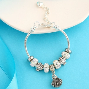 Macro detail of silver plated heart charm and seashell beads on snake chain bracelet