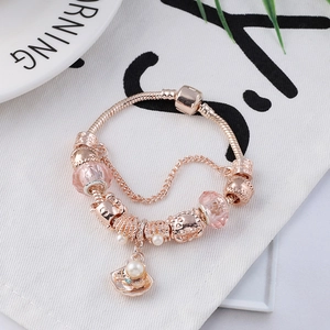 Roze kristallen kralenarmband met roségouden schelp en parelhangers op witte stof