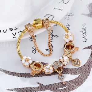 Goldenes Bettelarmband mit weißen Emaille-Blumen und einem herzförmigen Schlüsselanhänger