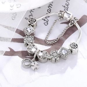 Silver charm bracelet with four-leaf clover, rose charms, and cubic zirconia crystals