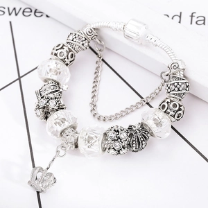 Detailed macro of a silver snake chain bracelet featuring a sparkling crown charm and crystal beads