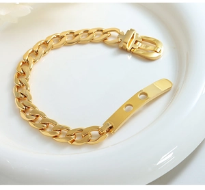 Nahaufnahme des goldenen Gliederkettenarmbands mit Gürtelschnalle auf weißem Teller