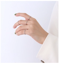 Dettaglio di anelli minimalisti in argento sulla mano con polsino di giacca bianca