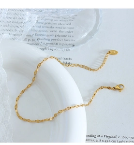 Close-up of gold fish scale chain anklet with K18 tag and lobster clasp on white lace