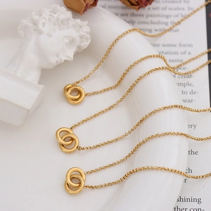 Tres collares de cadena con colgante de doble anillo dorado sobre base artística en blanco