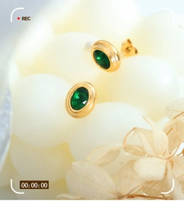 Vista macro de pendientes ovalados dorados con circonitas verdes y diseño retro elegante