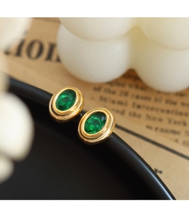 Primer plano de pendientes ovalados dorados con piedras verde esmeralda facetadas