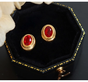 Primer plano de pendientes de titanio dorado con circón rojo en caja de terciopelo