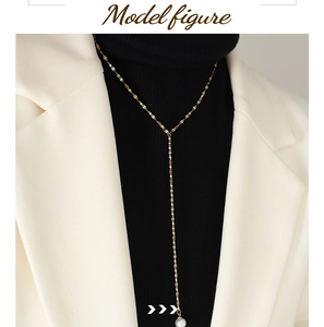 Detail van een gouden Y-vormige parelketting op een model met witte blazer