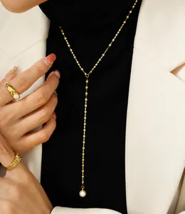 Detail van de gouden parel Y-ketting en getextureerde ring op model in wit zakelijk pak