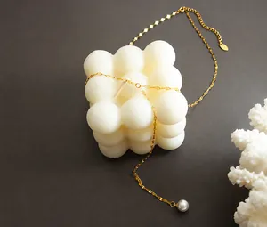 Detail van gouden vismond ketting met witte parelhanger op een witte kaars