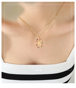 Detail der eleganten Goldkette mit Buchstaben N Anhänger und bunten Zirkoniasteinen am Model