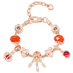 Detail of rose gold charm bracelet with red crown and tree of life feather pendant