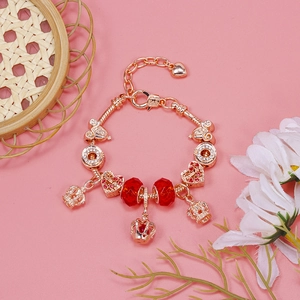 Detail of rose gold charm bracelet with crown pendant and red crystal beads on pink background