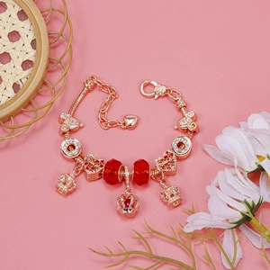 Macro shot of rose gold charm bracelet with red beads and crown heart pendants