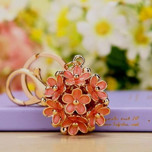 Floral sphere keychain with peach enamel blossoms and gold lobster clasp on lavender book