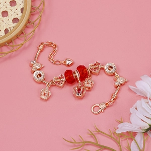 Golden crown and heart charm bracelet with red glass beads on a soft pink backdrop